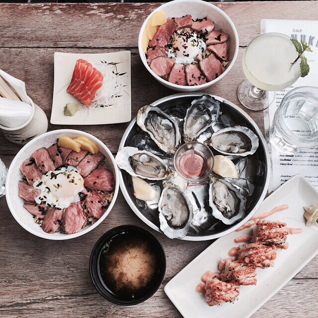 Tanuki Raw happy hour table — donburi bowls, fresh oysters on ice, maki rolls and cocktail
